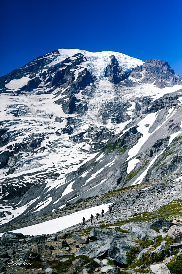 Mount Rainier's glaciers, with a line of hikers crossing the rocky slope below